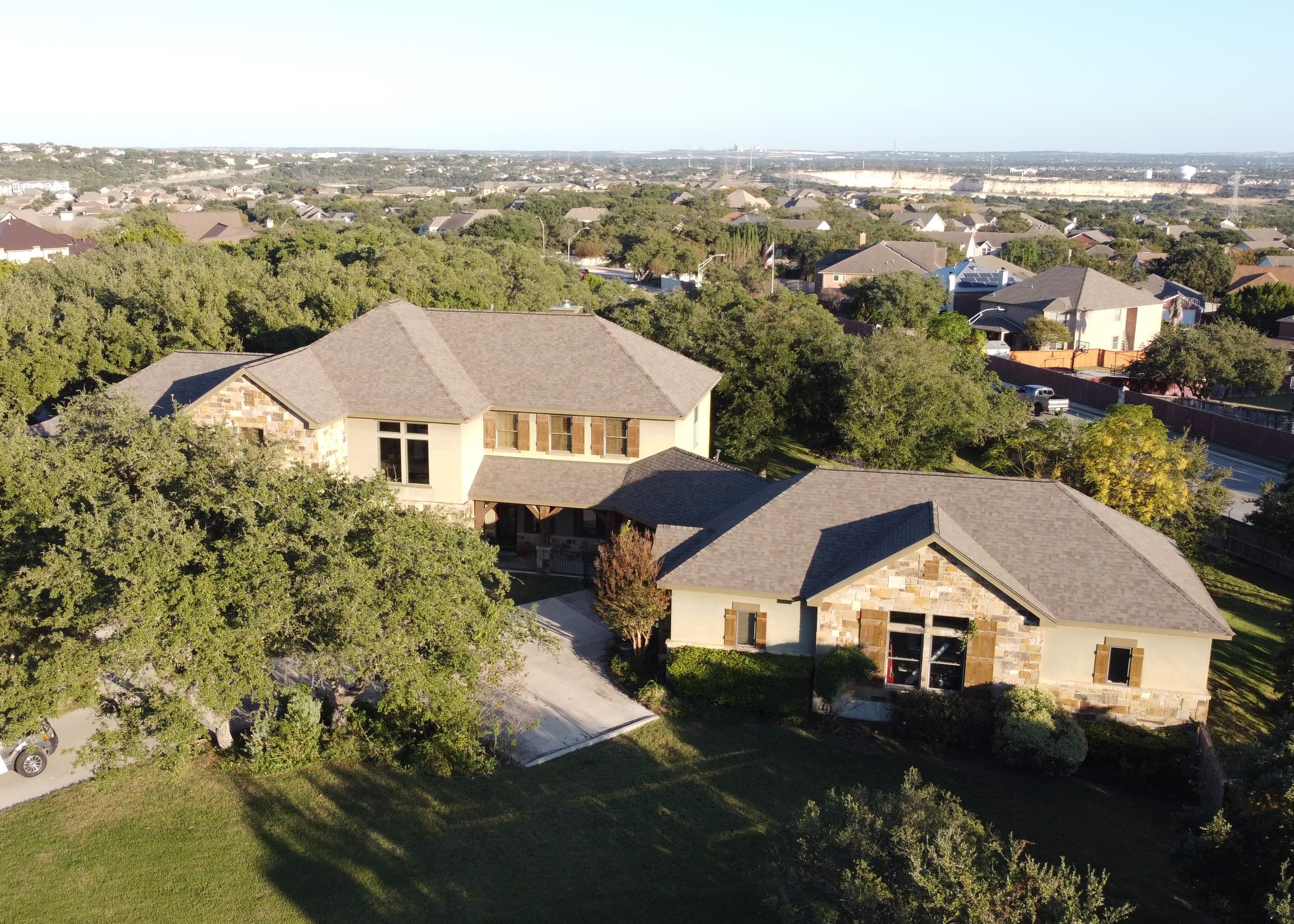Aerial view of a large stone and stucco suburban home surrounded by lush green trees.